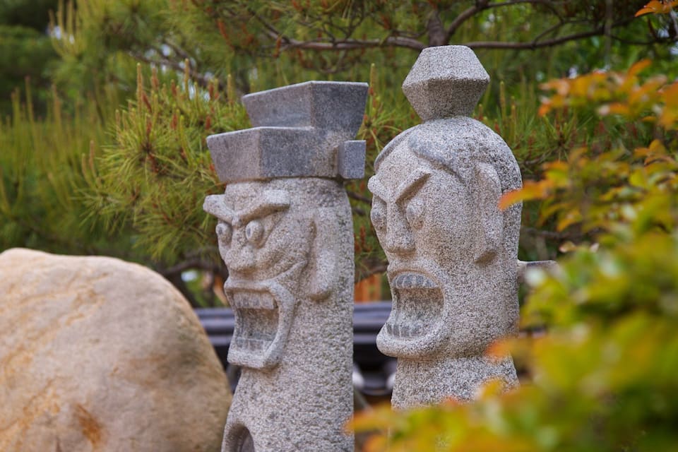 Estatuas de piedra en un jardín con árboles y una roca grande con inscripciones.