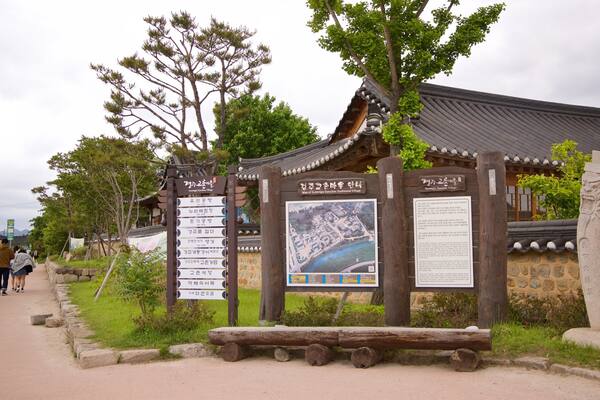 Eingang eines traditionellen koreanischen Dorfes mit hölzernem Schild und einem Pflasterweg.
