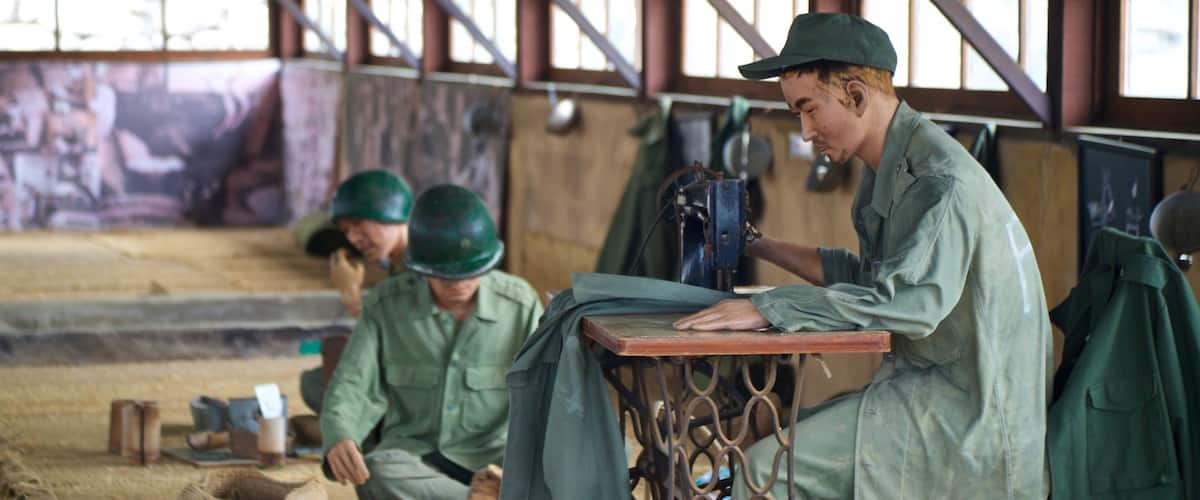 A workshop with workers in green uniforms and helmets, sewing machines, and a large window in the background.