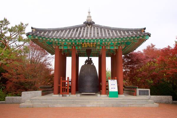 Un pavillon coréen traditionnel, avec une grande cloche au centre, entouré d’un feuillage rouge.