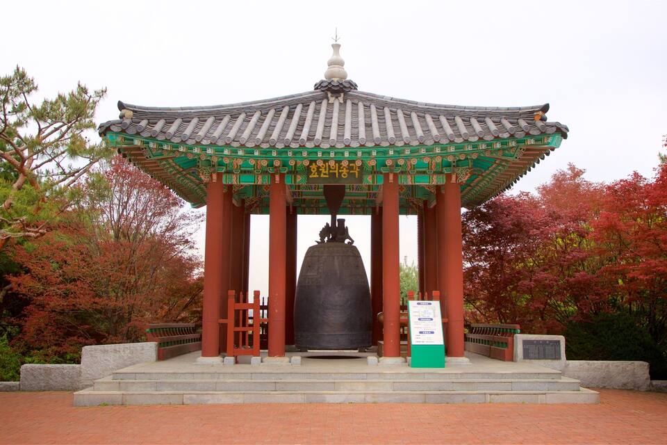 En traditionel koreansk pavillon med en stor klokke i midten, omgivet af rød vegetation.