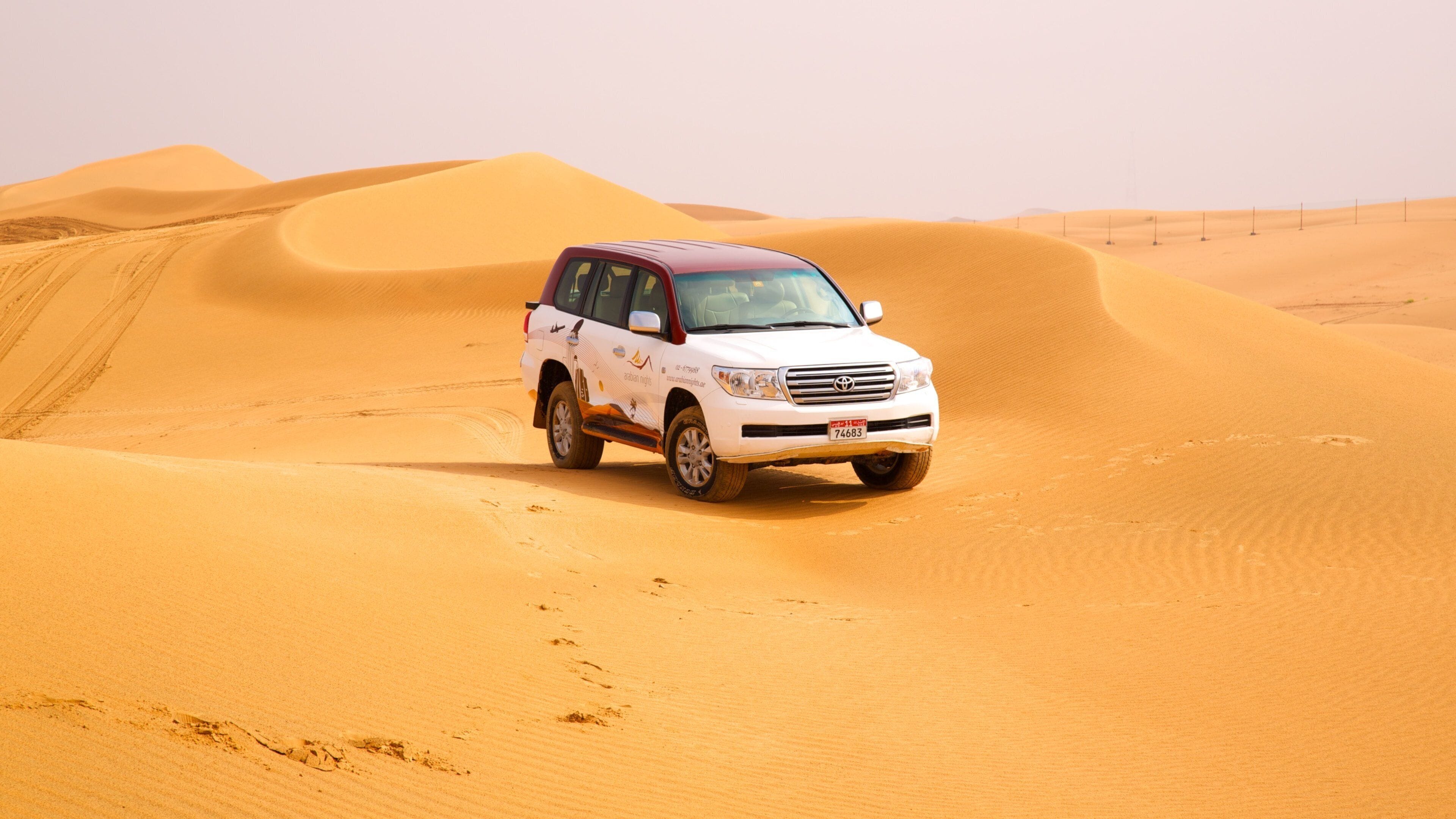 A white SUV driving through a desert with sand dunes.