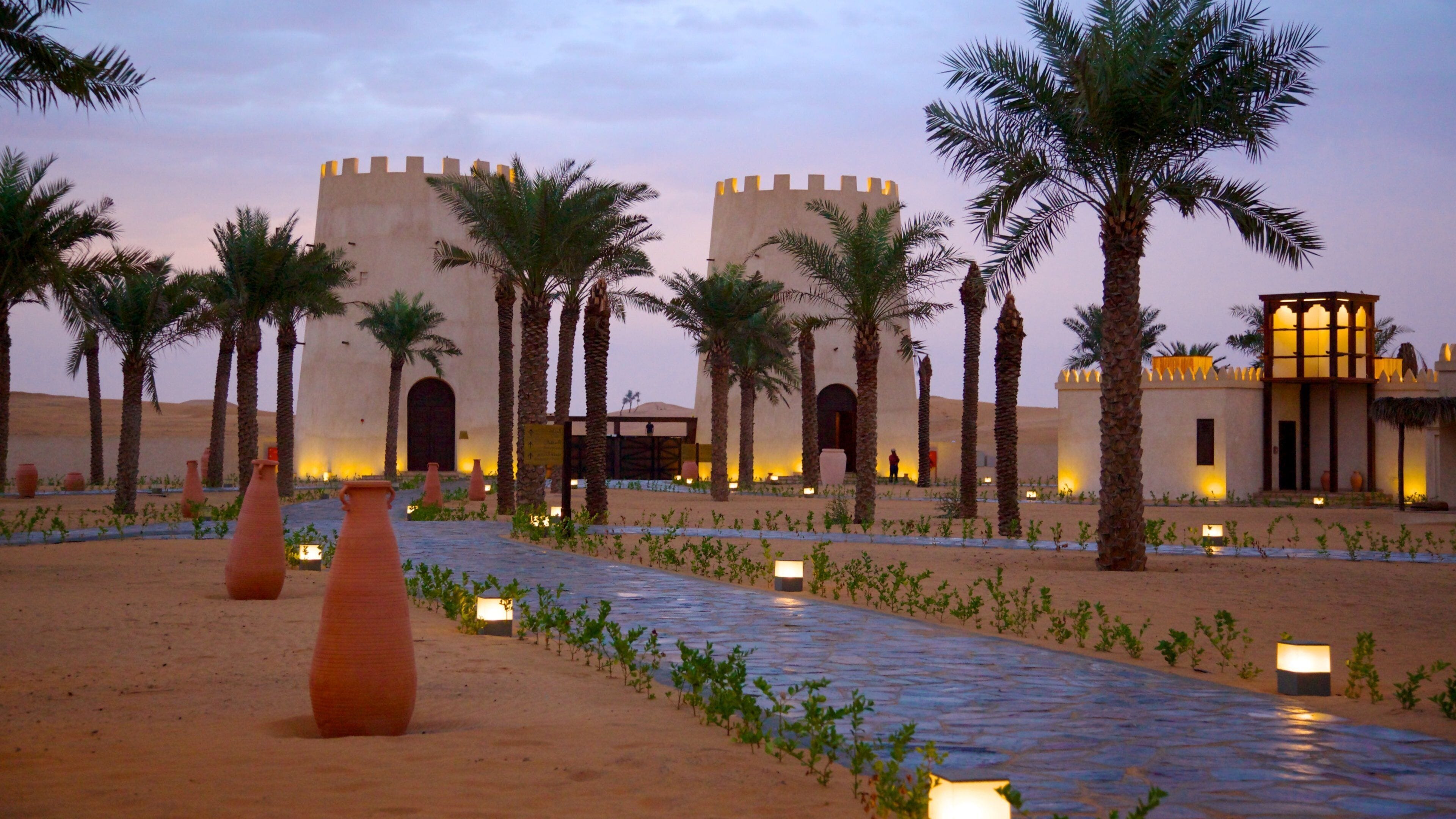 A desert landscape with palm trees and a building with two towers.