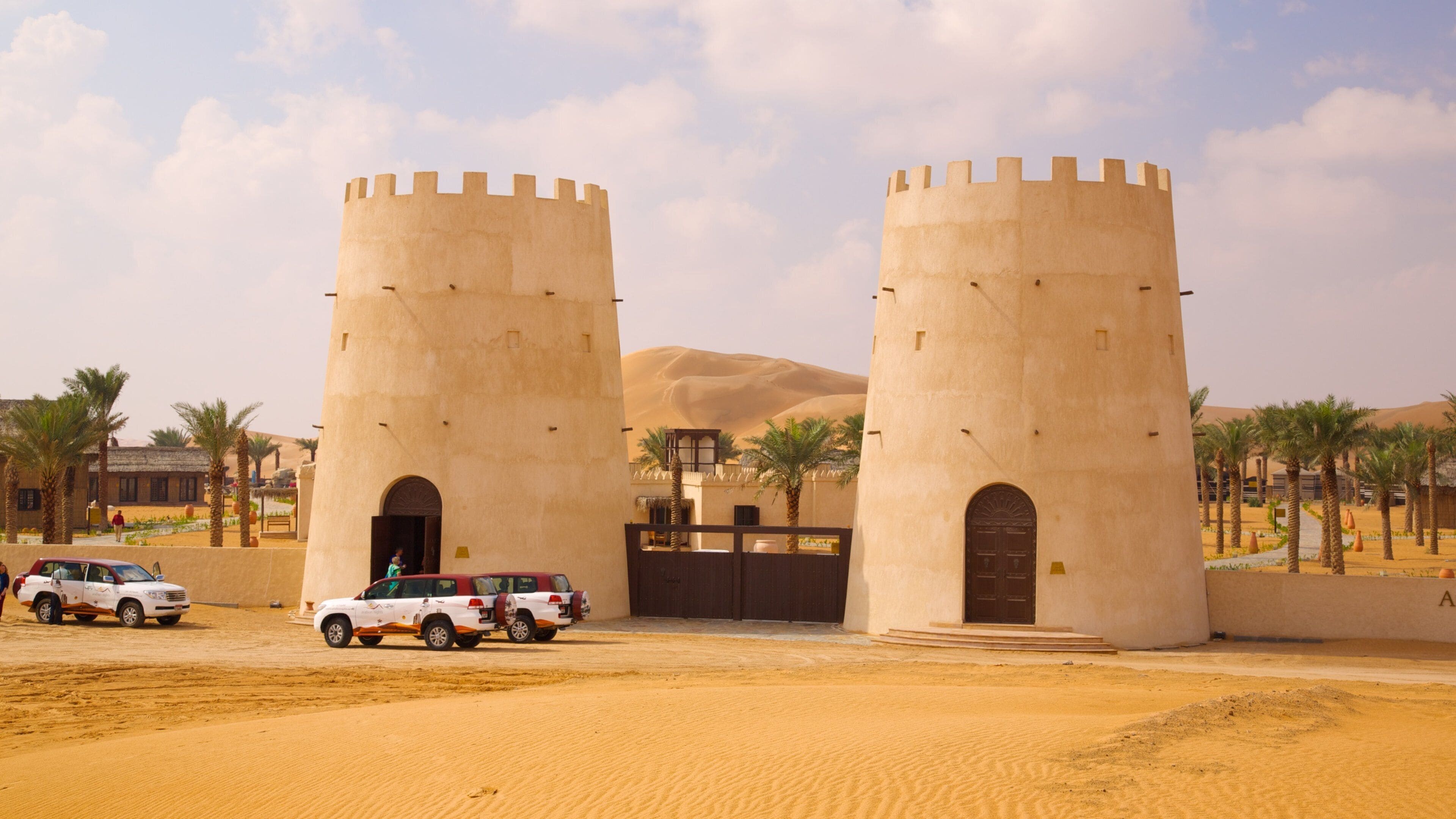 A desert landscape with two large towers and a white SUV parked in front.