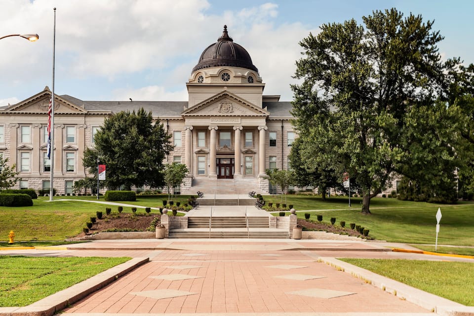 A large, historic building with a dome and columns, surrounded by well-maintained lawns and trees.