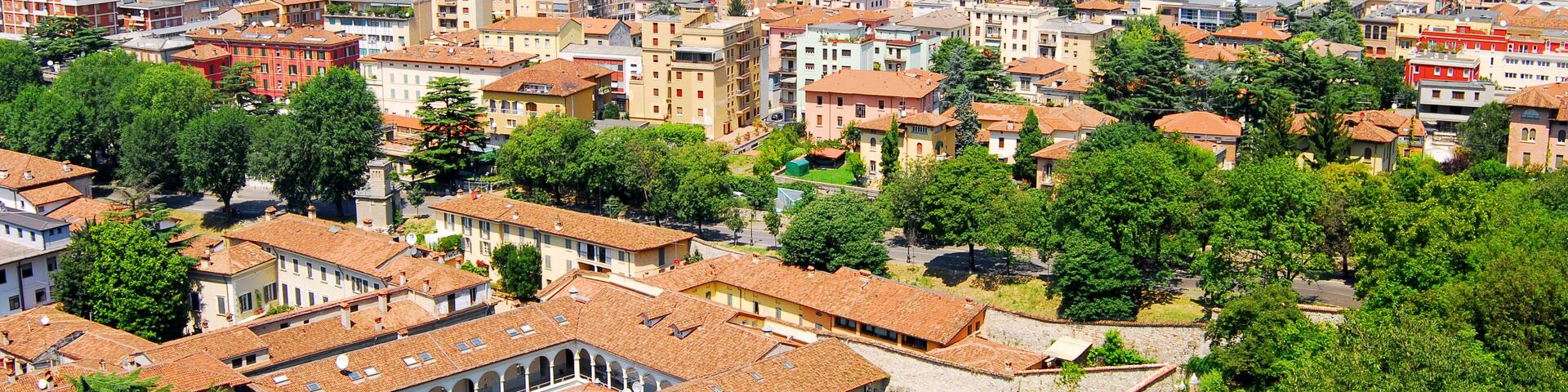 A cityscape with a mix of historic and modern buildings, surrounded by lush greenery and mountains in the background.