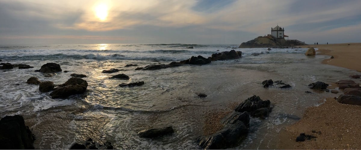 A beach with rocks, waves, and a lighthouse.
