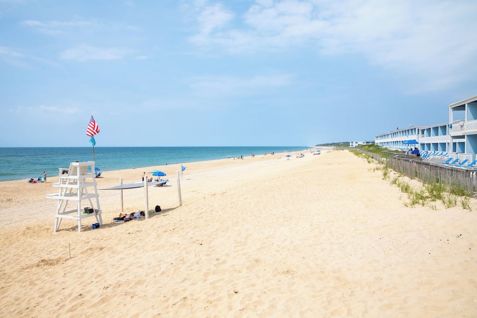 A beach with a lifeguard tower, American flag, and a row of beachside buildings.