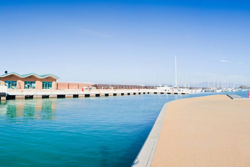 Puerto deportivo con barcos, un faro y un edificio de techo verde.