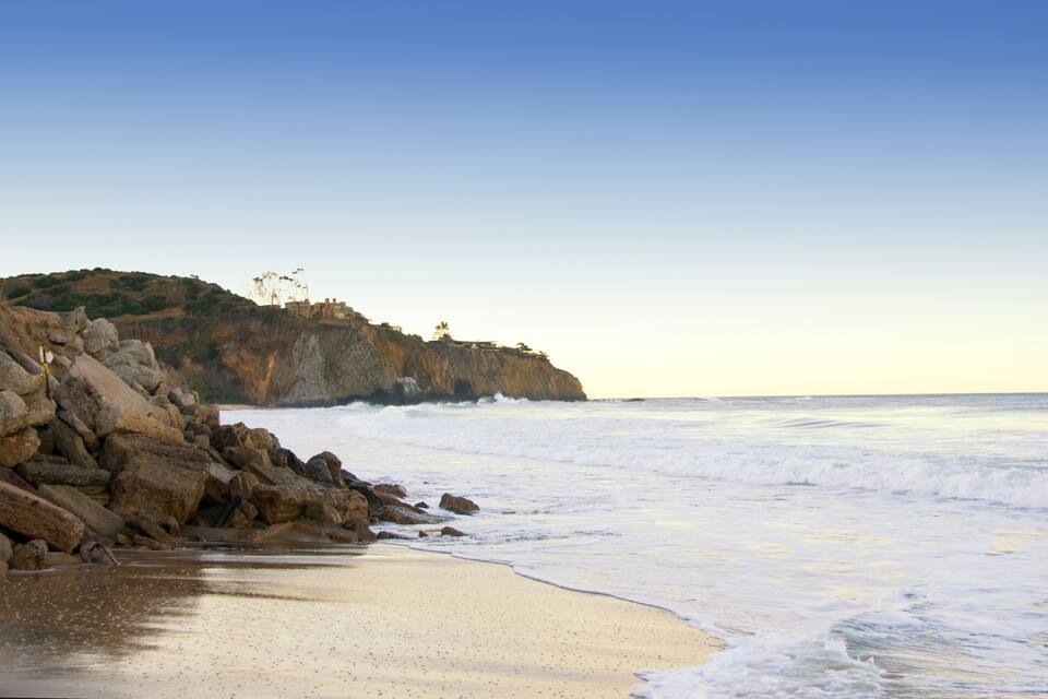 Costa rocosa con olas rompiendo en la orilla y un acantilado con vegetación escasa.