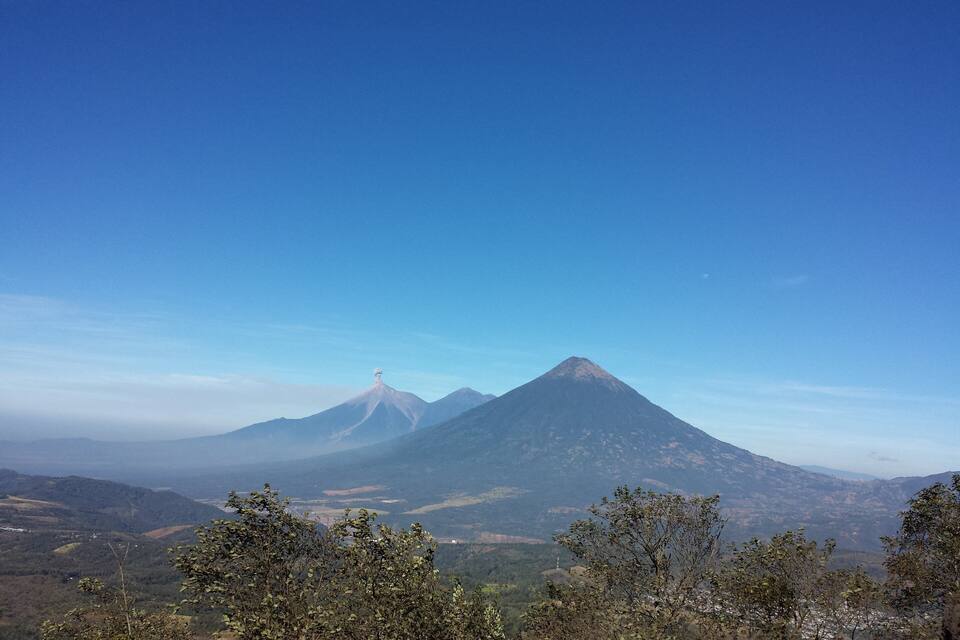 A mountain landscape with a prominent peak, a clear sky, and surrounding vegetation.