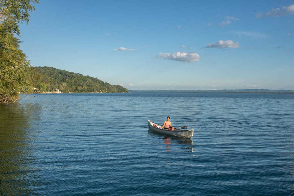A calm lake with a person in a canoe, surrounded by trees and distant hills.