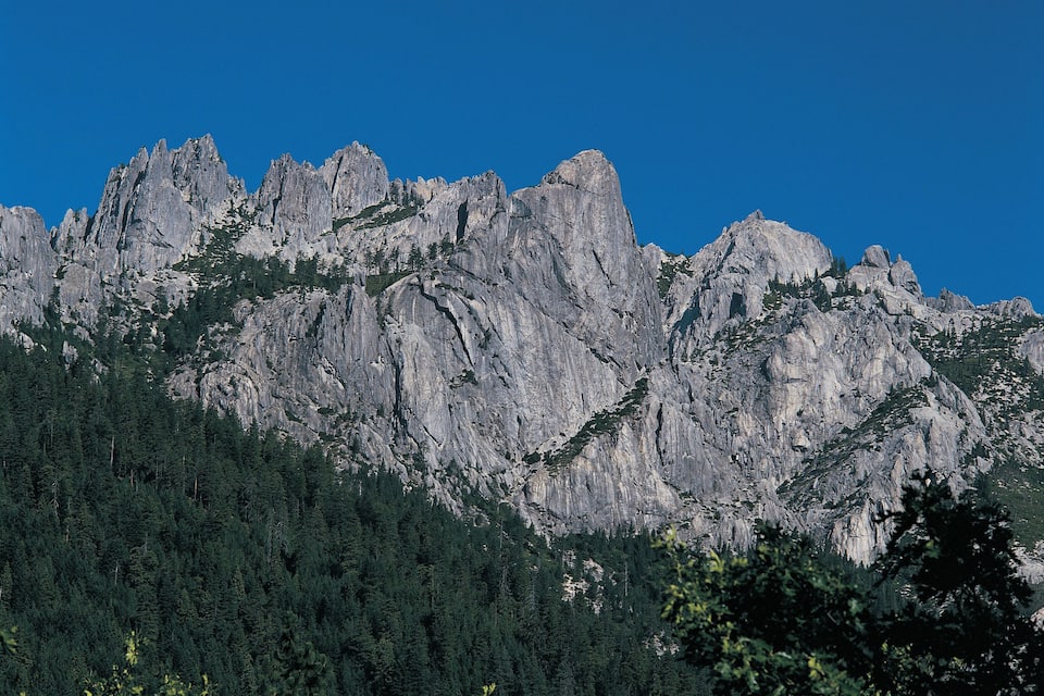 Een ruig berglandschap met steile, rotsachtige toppen en dichte bebossing.