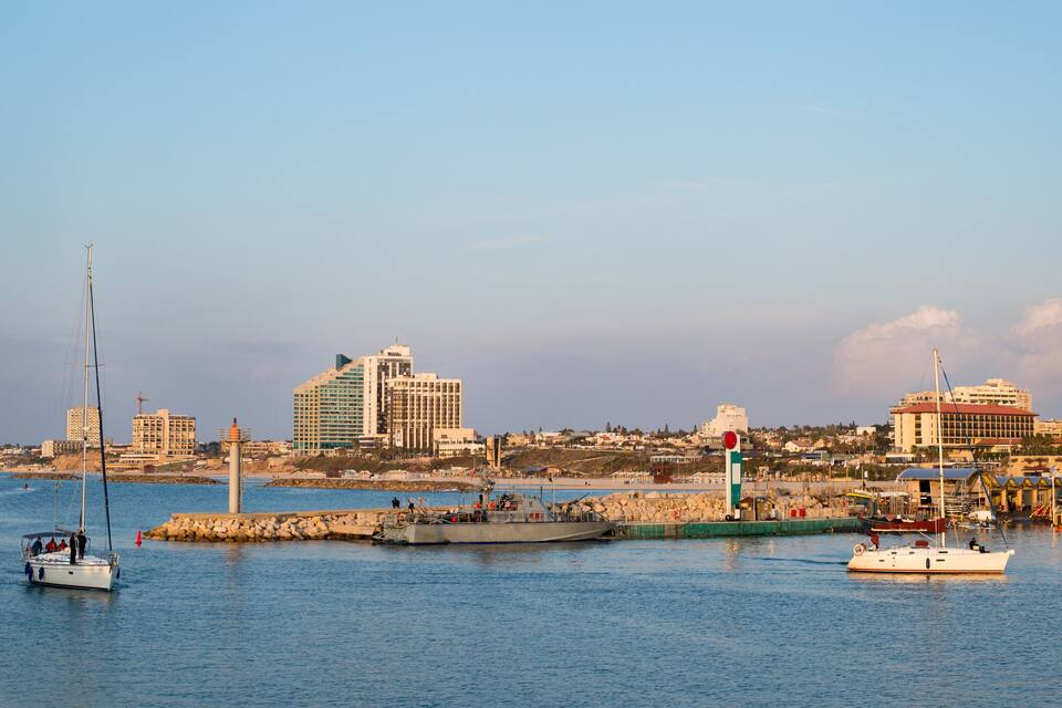 Um porto com barcos, um farol e um horizonte urbano com edifícios.