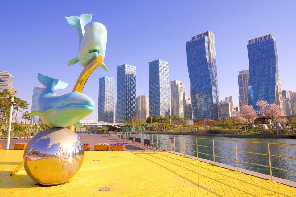 Eine Skulptur, die einen Wal und einen Vogel auf einer gelben Plattform an einem Fluss zeigt, im Hintergrund Hochhäuser.