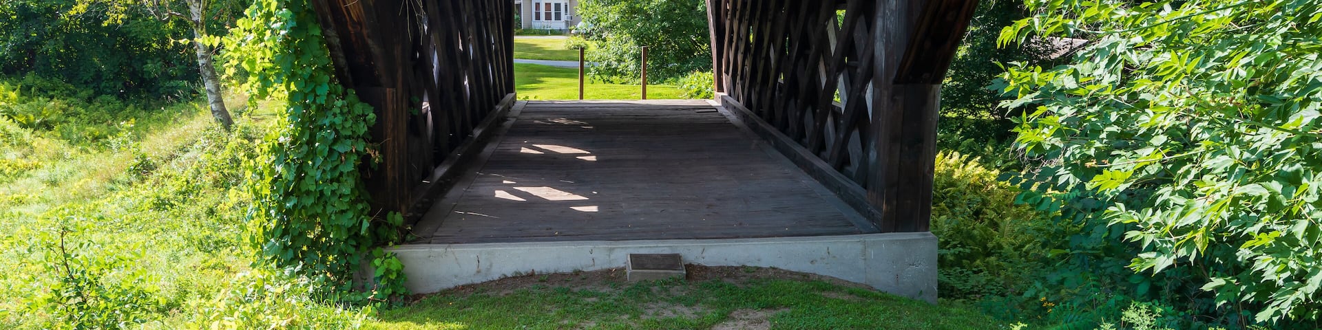 West end of the Baltimore covered bridge is an old wooden bridge located in Springfield Vermont with dark weathered wood located next to the Eureka one-room schoolhouse. Summer day in full sun.