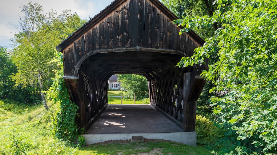 West end of the Baltimore covered bridge is an old wooden bridge located in Springfield Vermont with dark weathered wood located next to the Eureka one-room schoolhouse. Summer day in full sun.