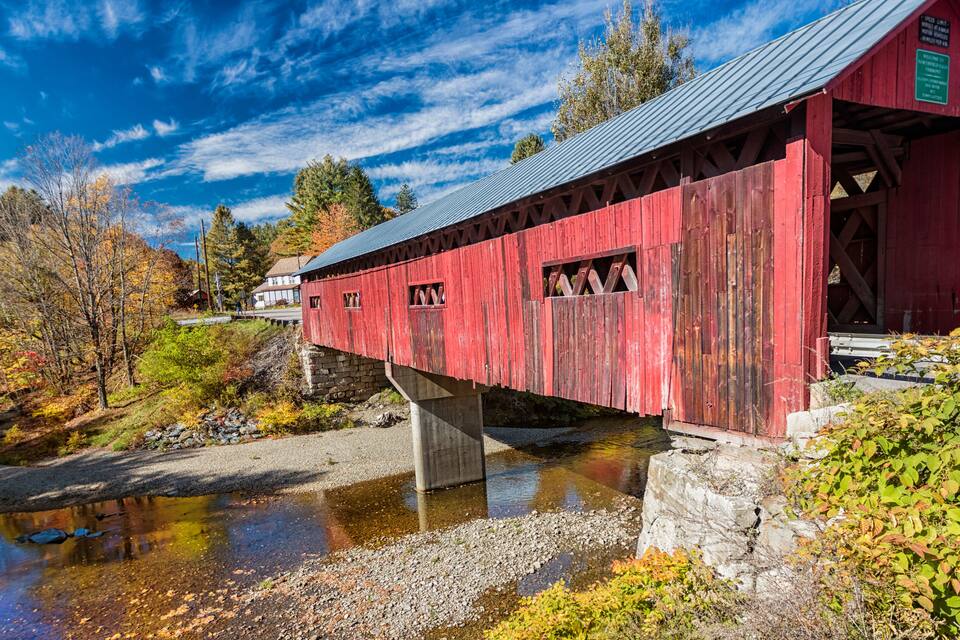 A red covered bridge over a river with autumn foliage.