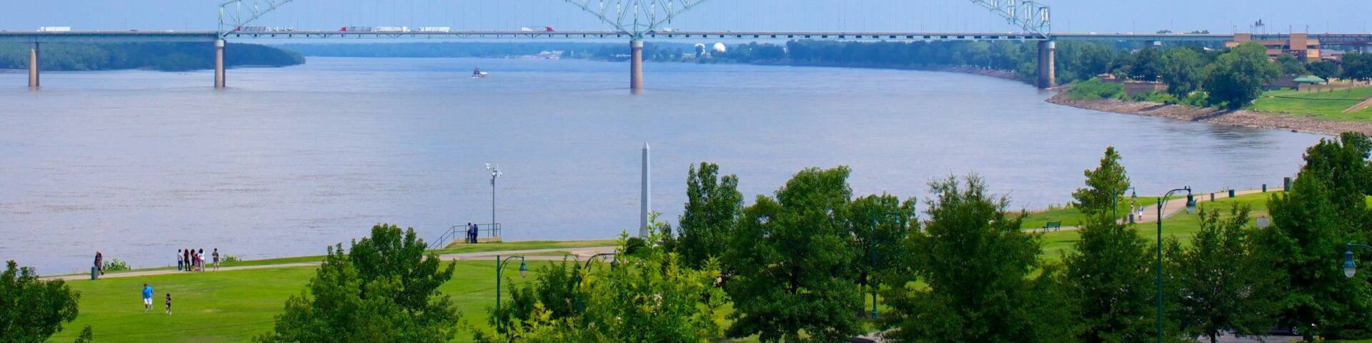 A large suspension bridge over a river with a park in the foreground.