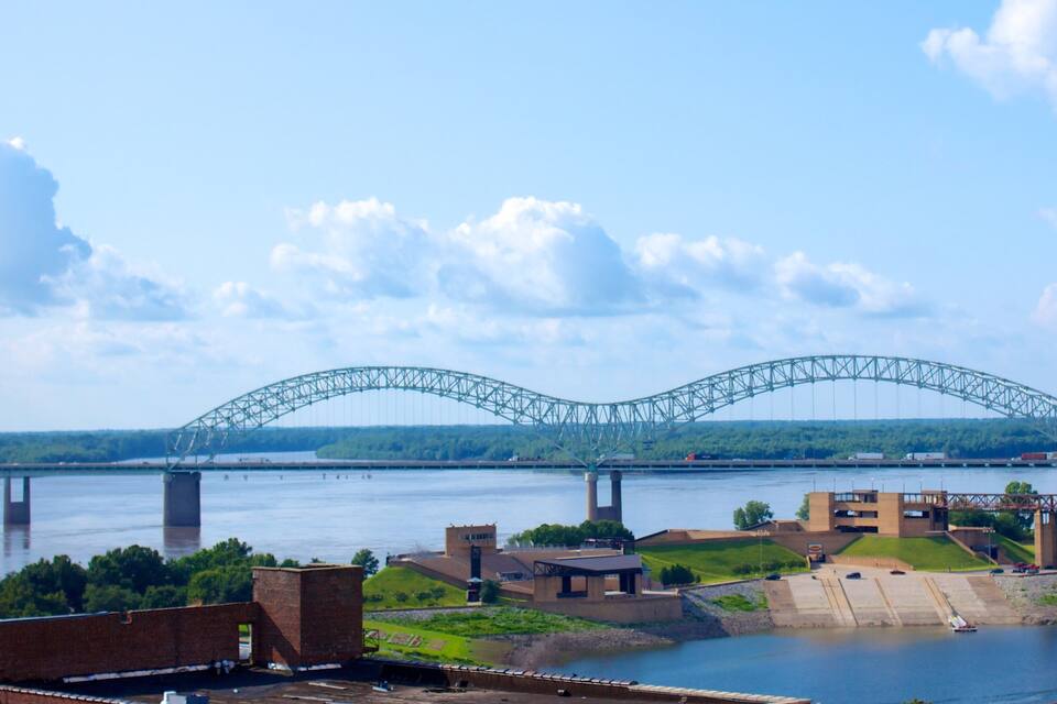 A large steel bridge spanning a river with a cityscape in the foreground.
