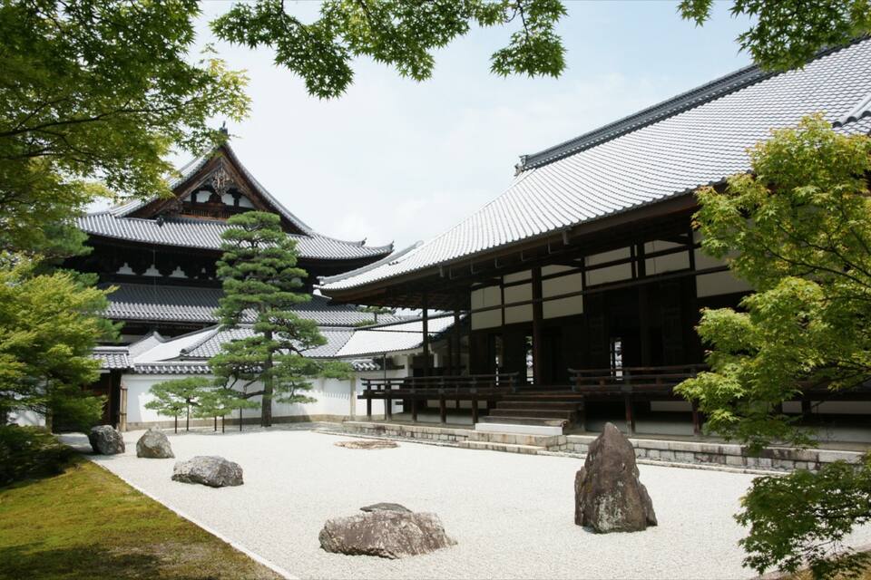 A traditional Japanese temple with a tiled roof, surrounded by trees and rocks.