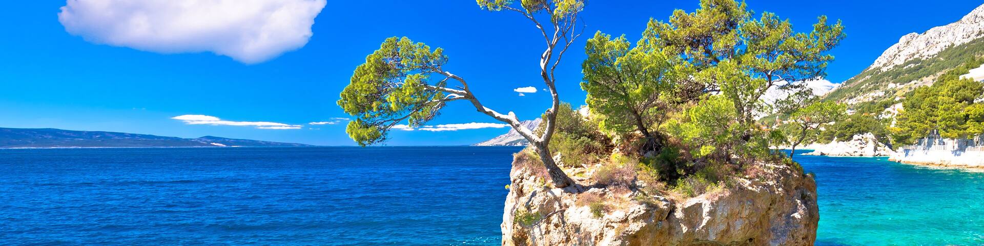A clear blue sea, a rocky island with trees, and distant mountains.