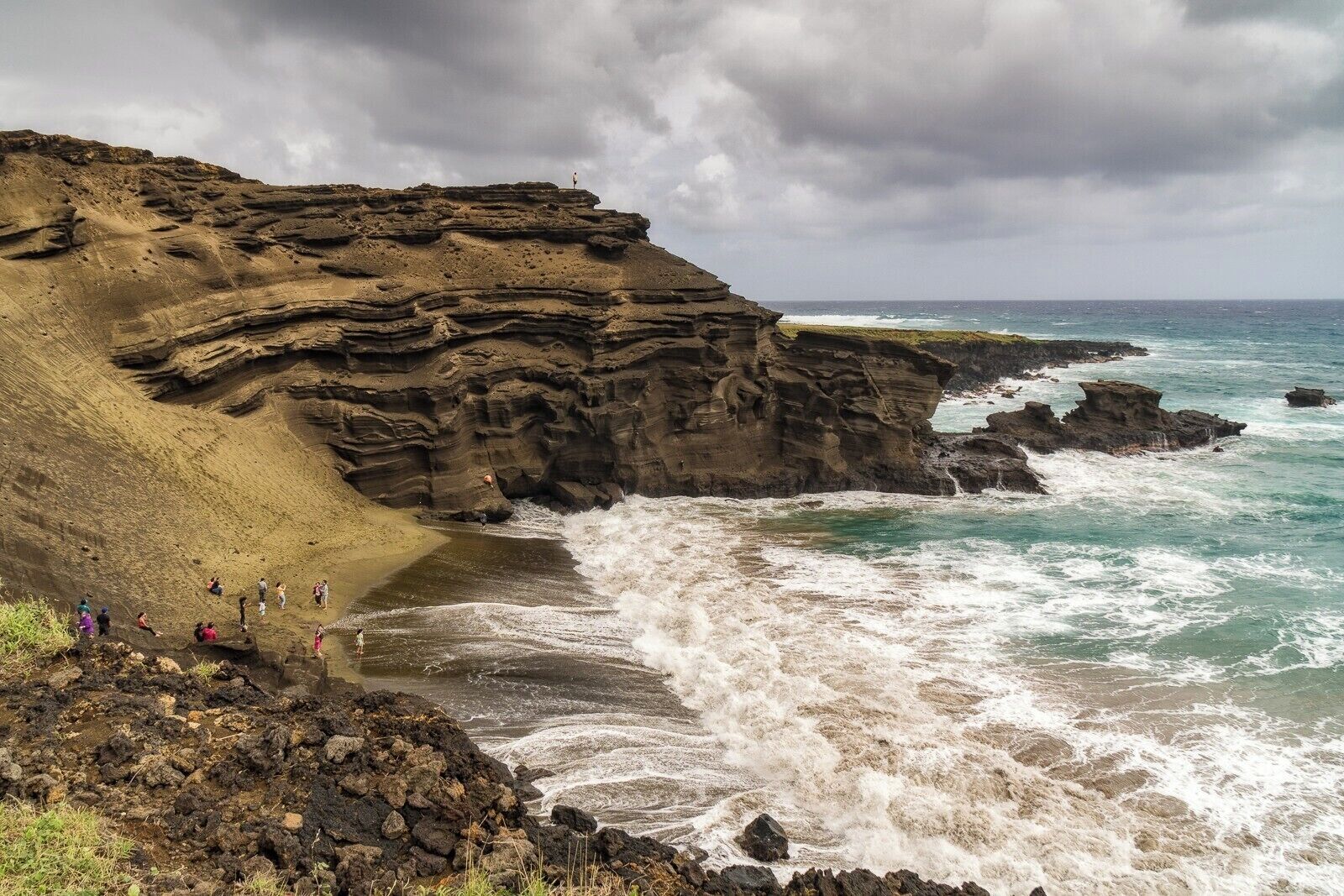 A rocky coastline with waves crashing against the shore and people walking along the beach.