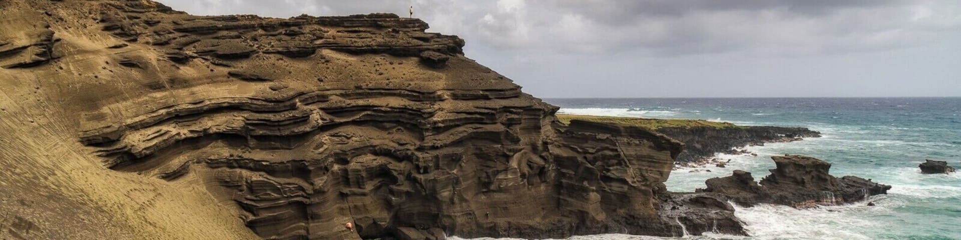 Una costa rocosa con olas rompiendo sobre la orilla y gente caminando por la playa.