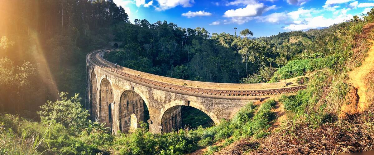 A stone bridge with arches over a river, surrounded by lush greenery and hills.
