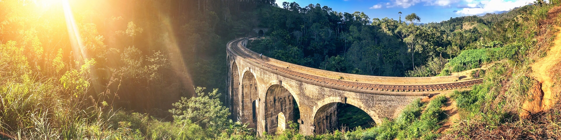 A stone bridge with arches over a river, surrounded by lush greenery and hills.