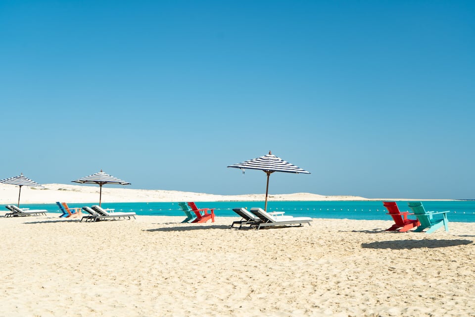 A beach with white sand, turquoise water, and several beach chairs and umbrellas.