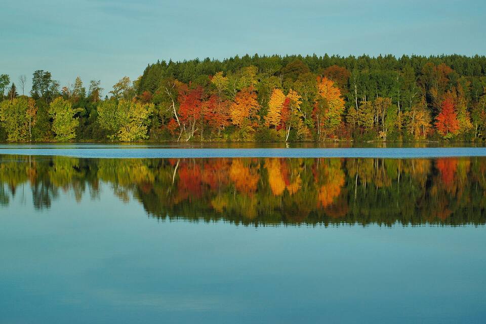 A calm lake with autumn-colored trees reflecting on the water.