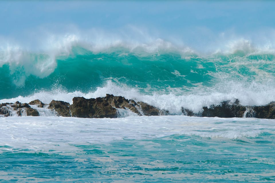 A large wave crashing against rocky coastline.
