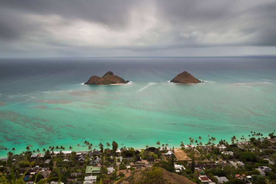 A coastal town with turquoise waters, two prominent rocky islands, and a dense cluster of houses.