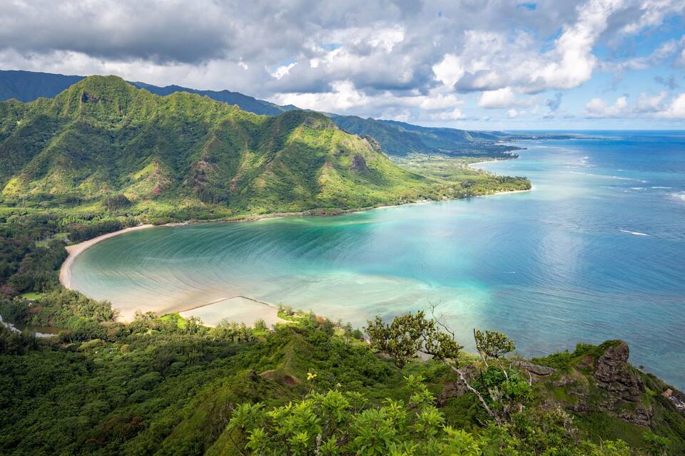 A coastal landscape with lush green hills, a sandy beach, and clear turquoise waters.