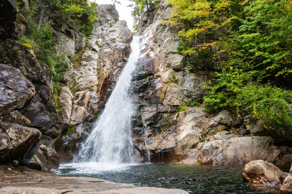 A waterfall cascading down a rocky cliff surrounded by lush greenery.