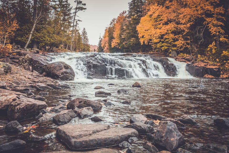 A waterfall surrounded by autumn-colored trees and rocky terrain.