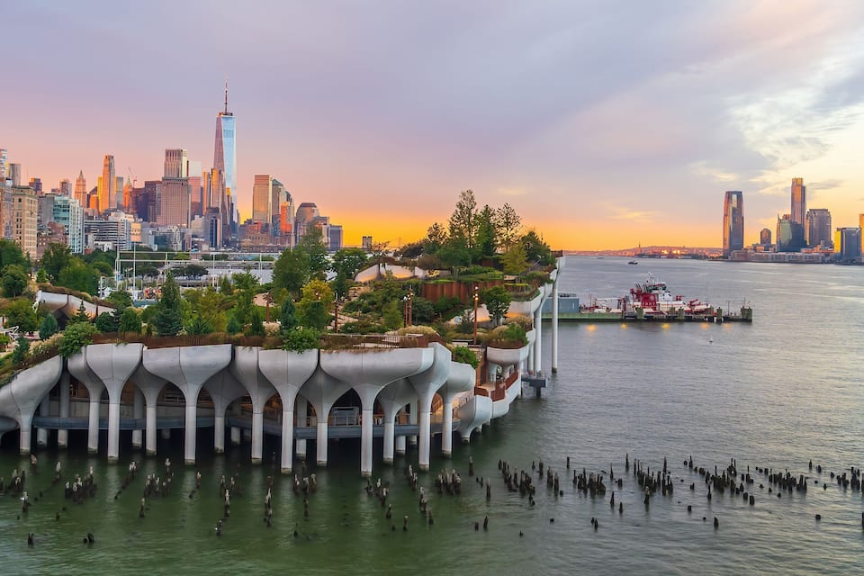 A waterfront cityscape with modern architecture, including a distinctive bridge with arches, a river with boats, and a skyline with tall buildings.