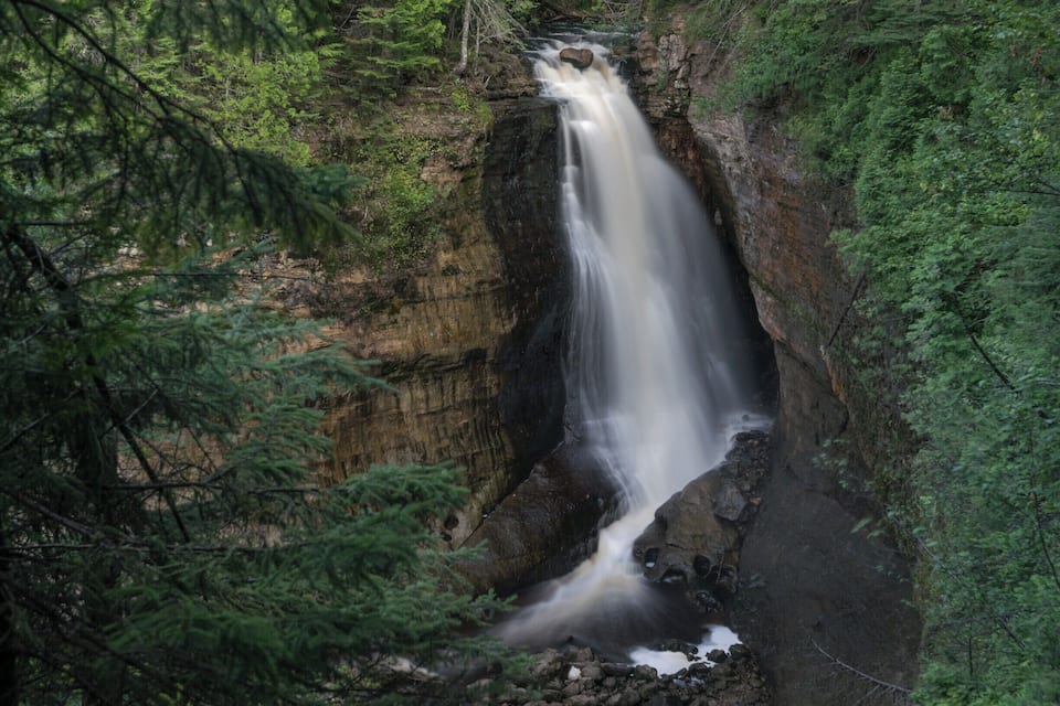 Una cascada que se precipita por un risco rocoso rodeado de un bosque denso.