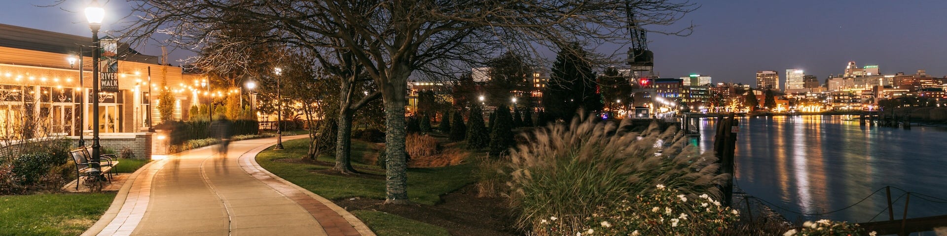 Un paseo junto al río de noche, con el horizonte de la ciudad al fondo.
