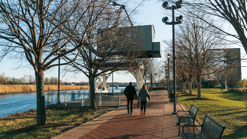 A park with a river, benches, and a covered walkway.