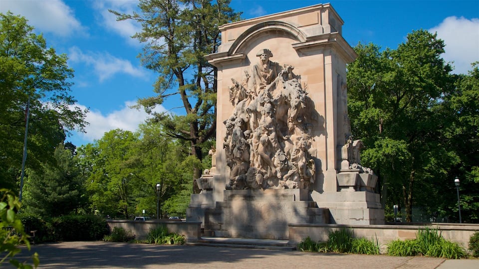 A large stone monument with intricate carvings, surrounded by trees and a paved area.