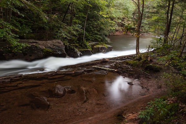 Late evening light reflects off a calm pool of water alongside a fast flowing stream at Seven Tubs Nature Area in Pennsylvania during Late Summer.