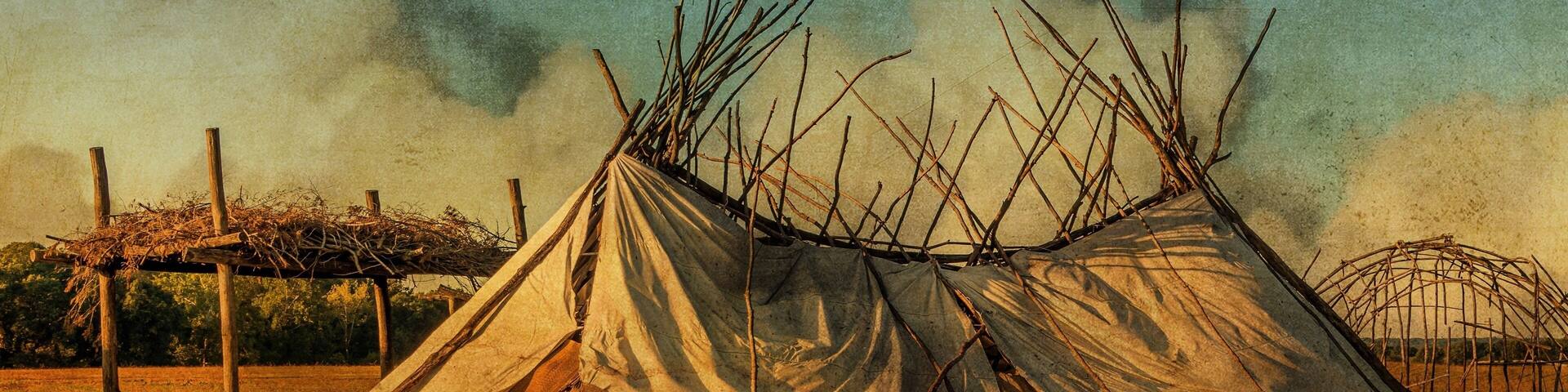 Un tipi tradicional con estructura de madera y cubierta de lona, rodeado por un campo de hierba y una valla de madera.