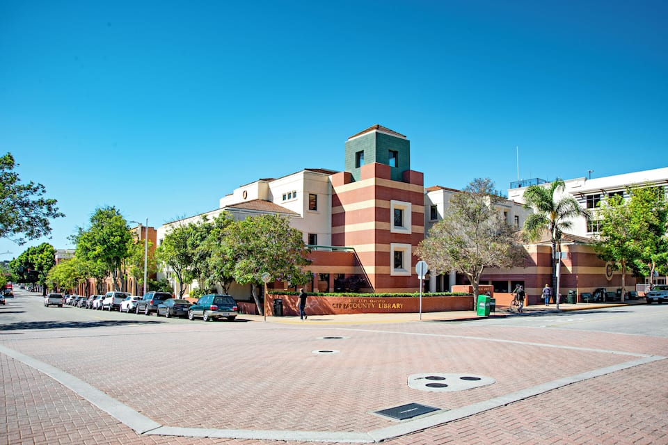 A library building with a distinctive red and beige facade, a green tower, and a clear blue sky.