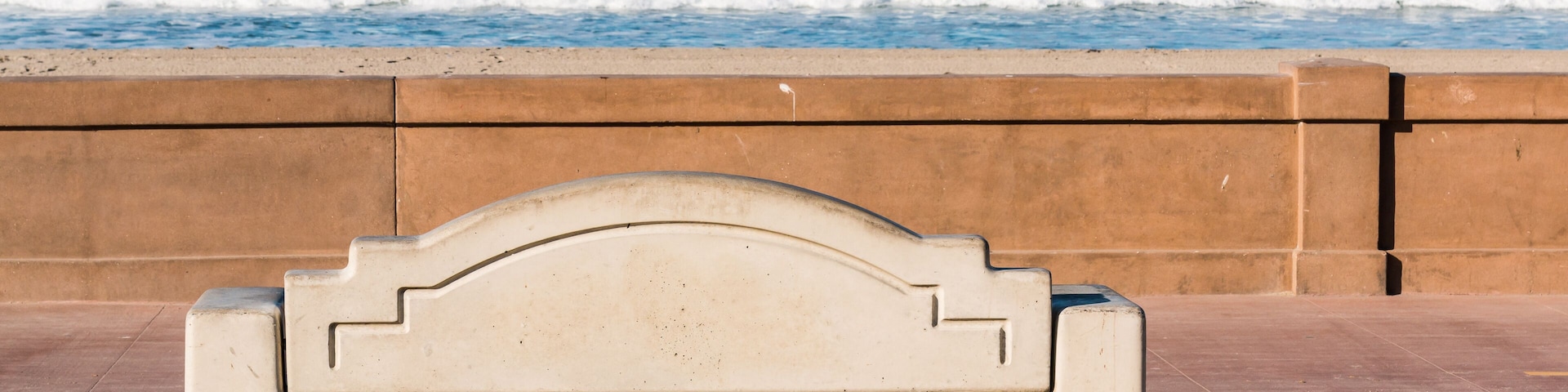 Bench on the Mission Beach boardwalk in San Diego, California with ocean waves in the background.