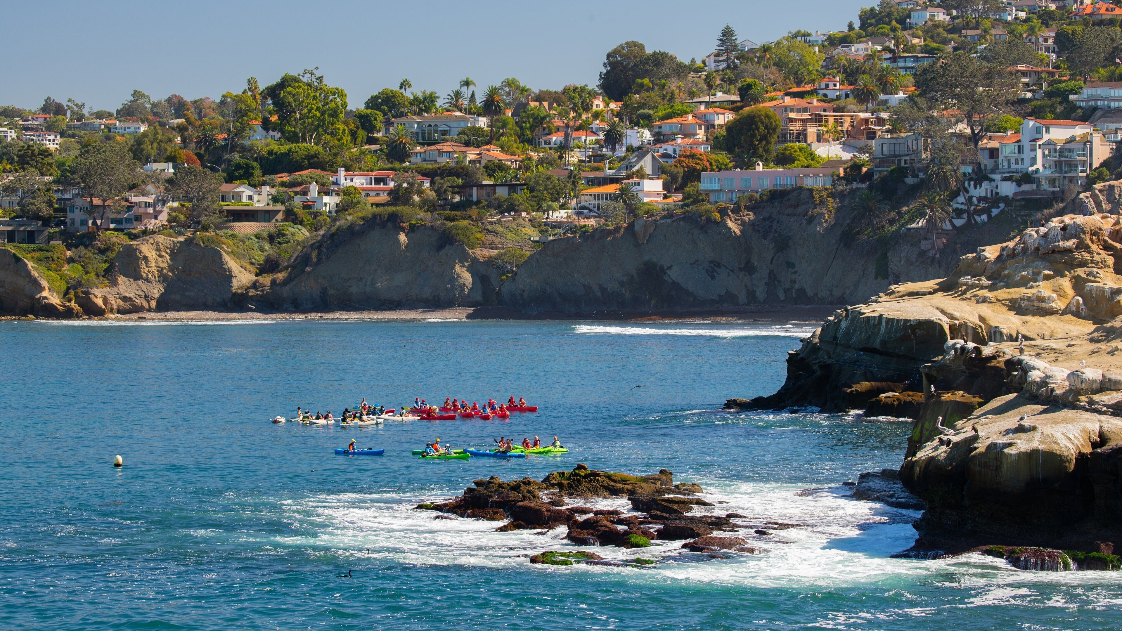 Une ville côtière avec des maisons construites sur une colline, un littoral rocheux et des gens qui font du kayak.