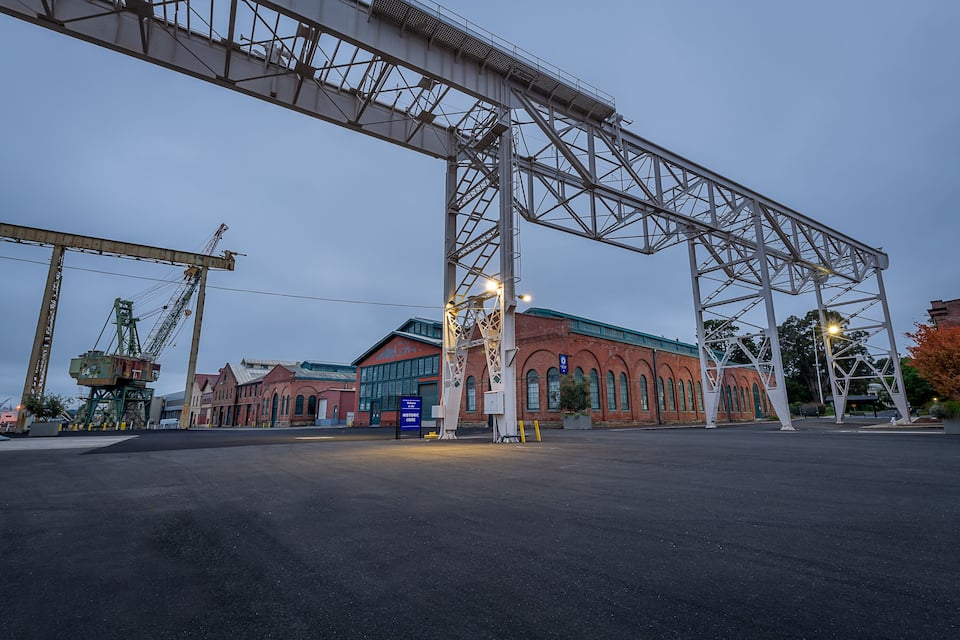 A large industrial area with a prominent bridge structure, a historic building, and a crane.