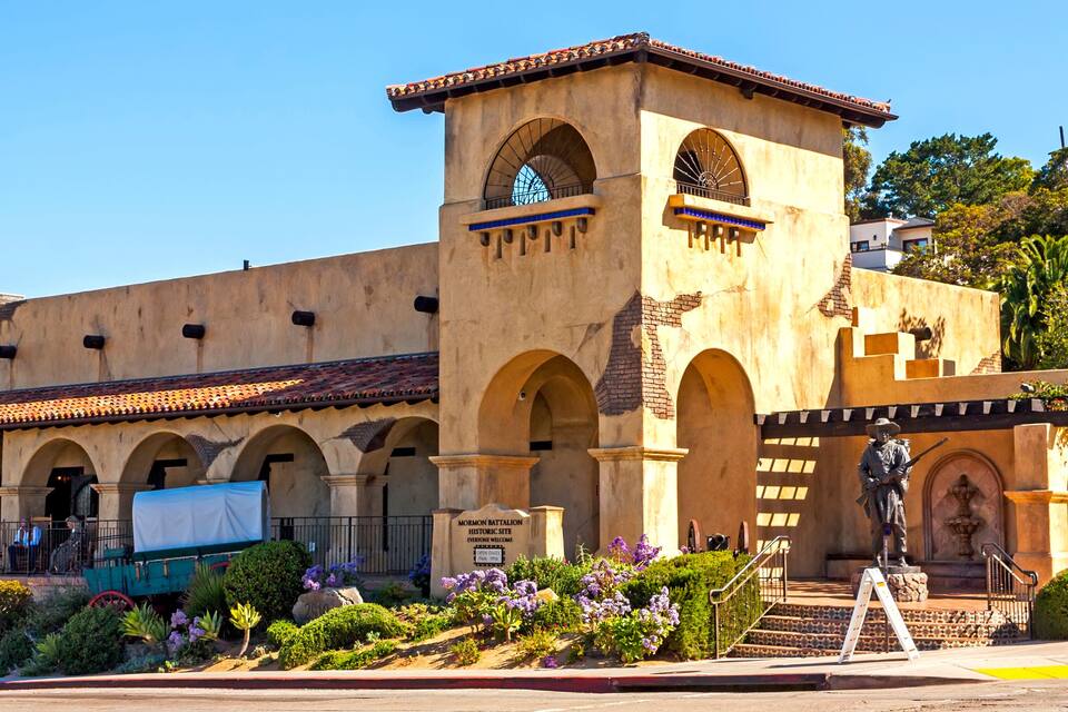 A historic building with arched walkways, a clock tower, and a statue.