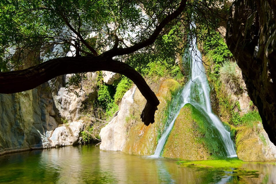 A waterfall cascading into a clear pool surrounded by rocky cliffs and lush greenery.